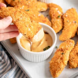 Dipping baked parmesan chicken tender into honey mustard dipping sauce.