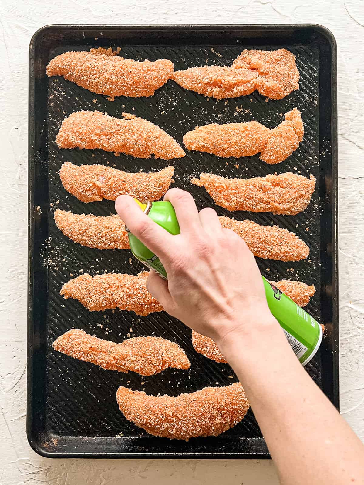 Spraying breaded chicken tenders with cooking spray.