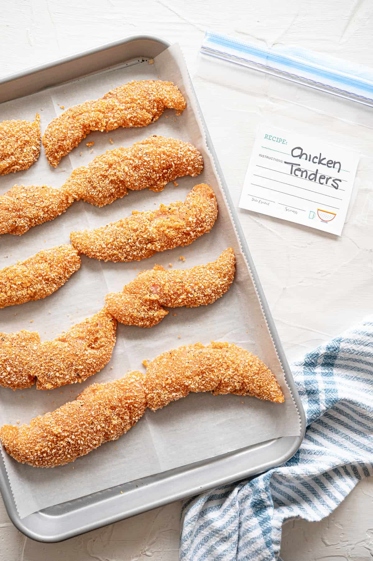 Breaded chicken tenders on a sheet pan ready to flash freeze.