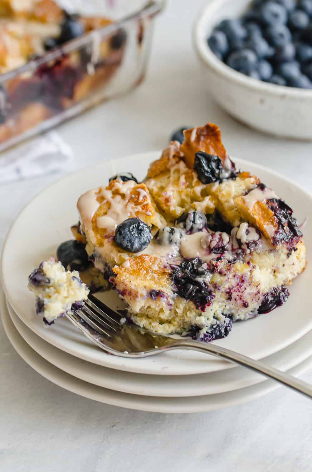 a serving of blueberry french toast casserole with vanilla glaze on a plate with a fork