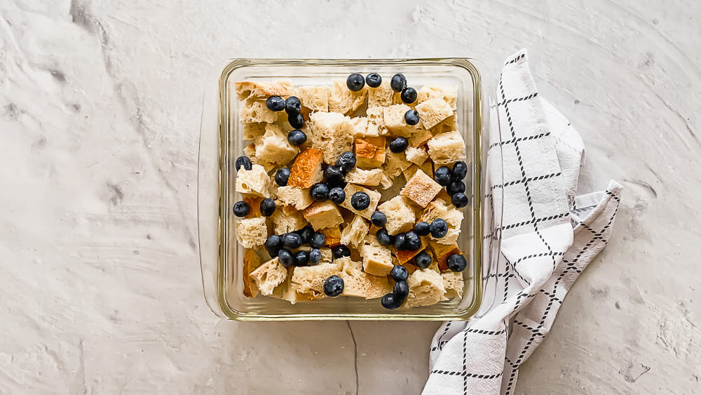 bread pieces and blueberries in a glass casserole dish with an egg mixture on top