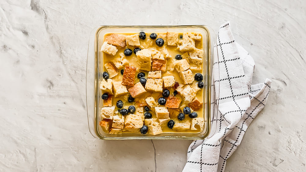bread pieces and blueberries in a glass casserole dish