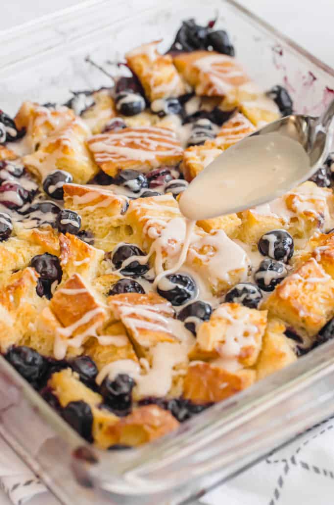 vanilla glaze being drizzled on top of a blueberry baked french toast casserole
