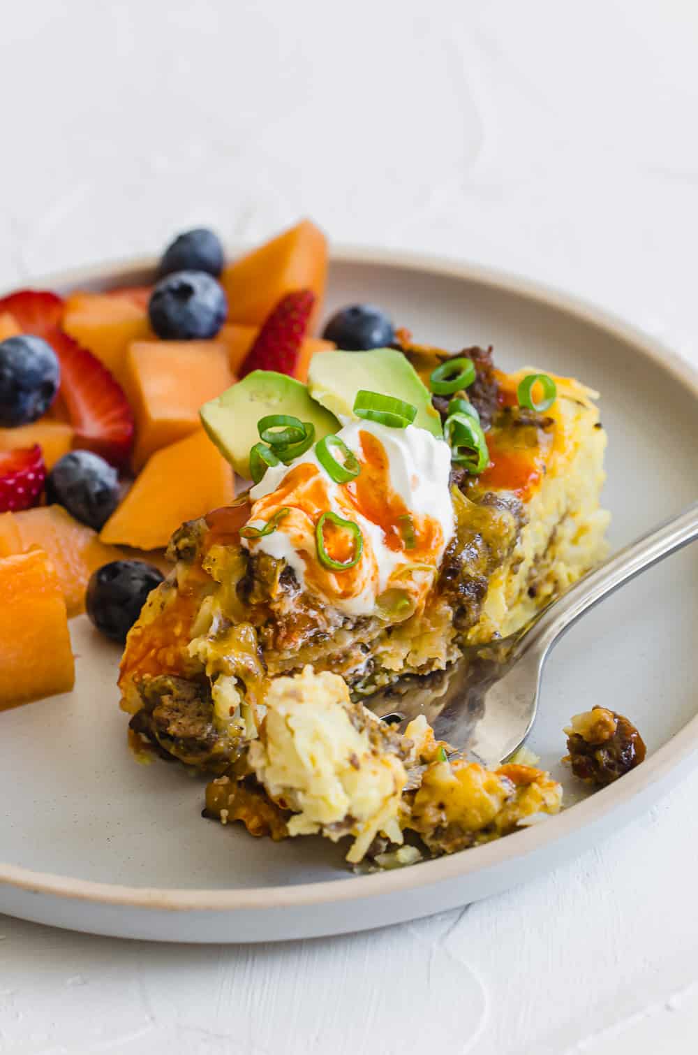 A slice of breakfast casserole on a plate with a fruit salad