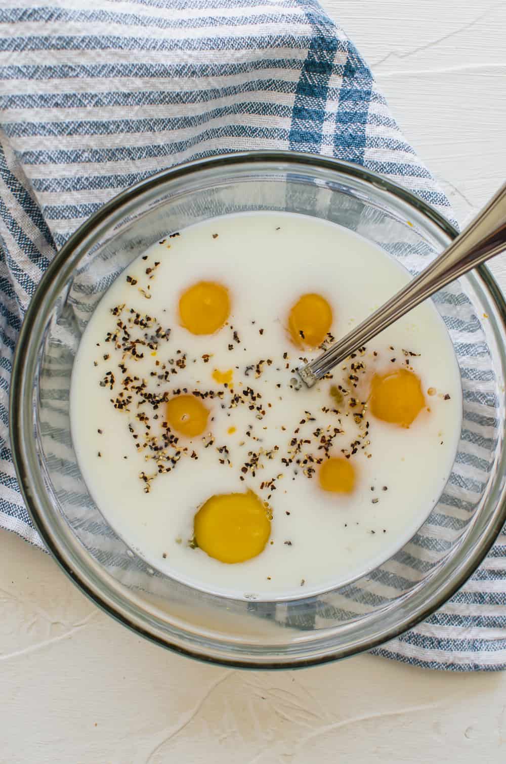 Eggs, milk, salt, and pepper in a bowl with a fork to be whisked together.