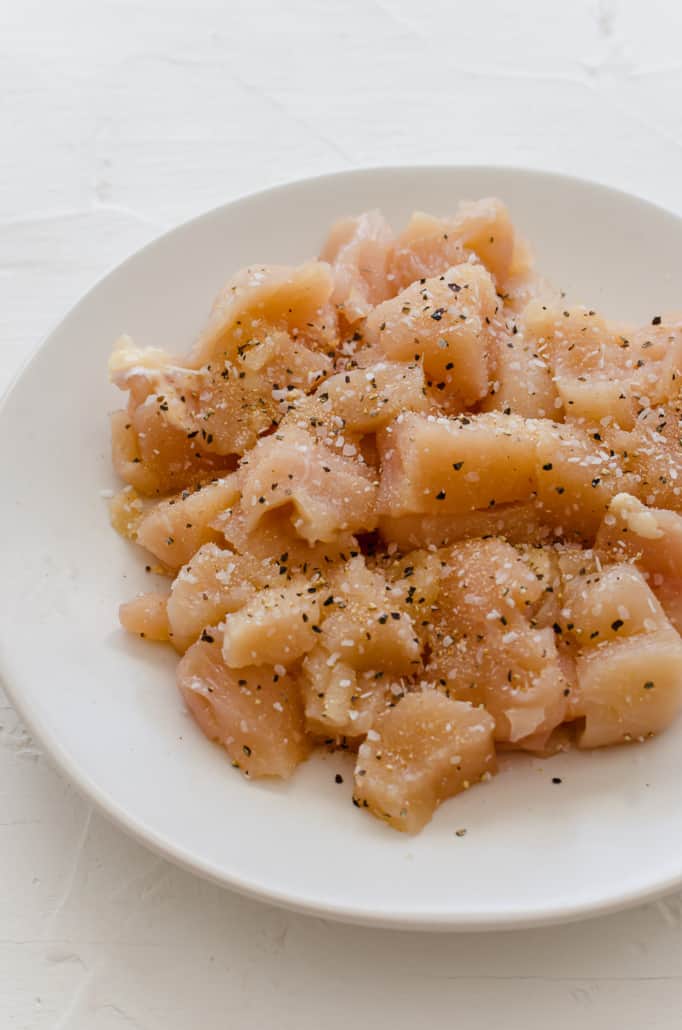 Raw, diced chicken that's been seasoned with salt and pepper on a plate