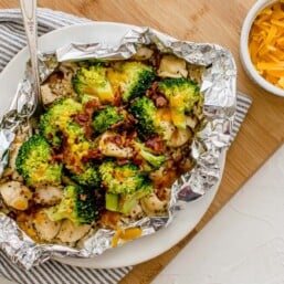 Chicken foil packet with broccoli, bacon, and rice open on a plate ready to eat.