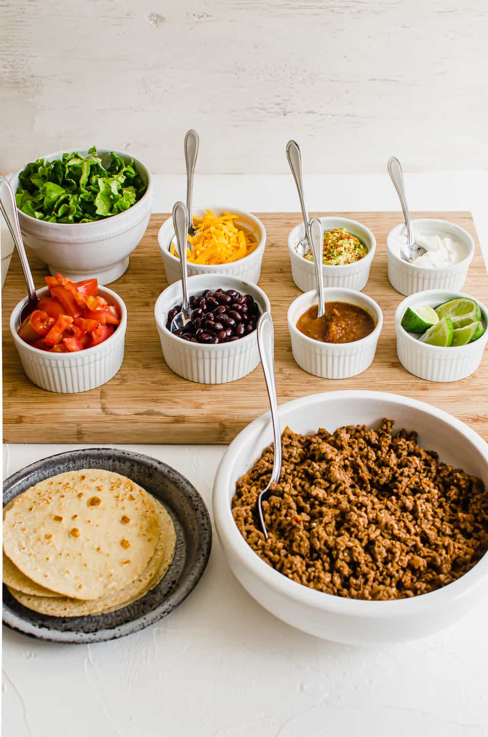 Taco bar set up with bowls of lettuce, tomatoes, sredded cheese, black beans, salsa, lime edges, sour cream, taco meat and tortillas.