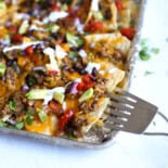 Baked nachos being served off a foil-covered sheet pan.