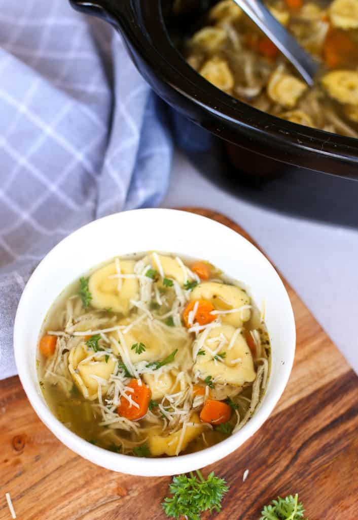 Chicken tortellini soup in a white bowl with a slow cooker in the background.