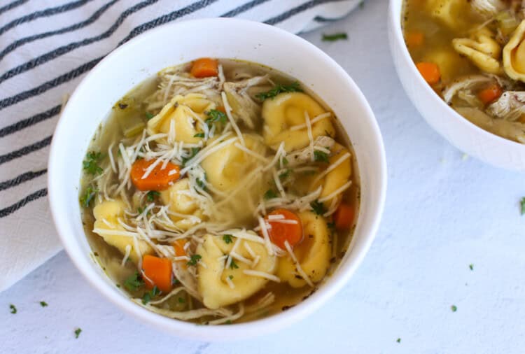 Chicken tortellini soup in a bowl with shredded Parmesan on top.