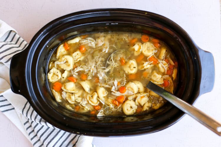 Easy crock pot chicken tortellini soup recipe in a slow cooker with ladle.