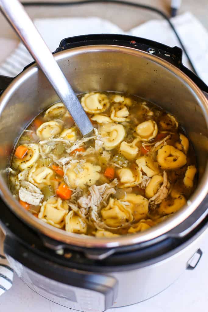 Chicken tortellini soup in the Instant Pot with a serving spoon.