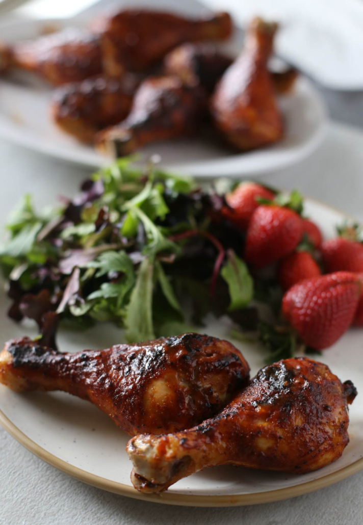 BBQ chicken drumsticks on a plate with a salad in the background