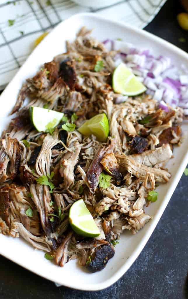 Carnitas de horno holandés en un plato blanco con rodajas de lima