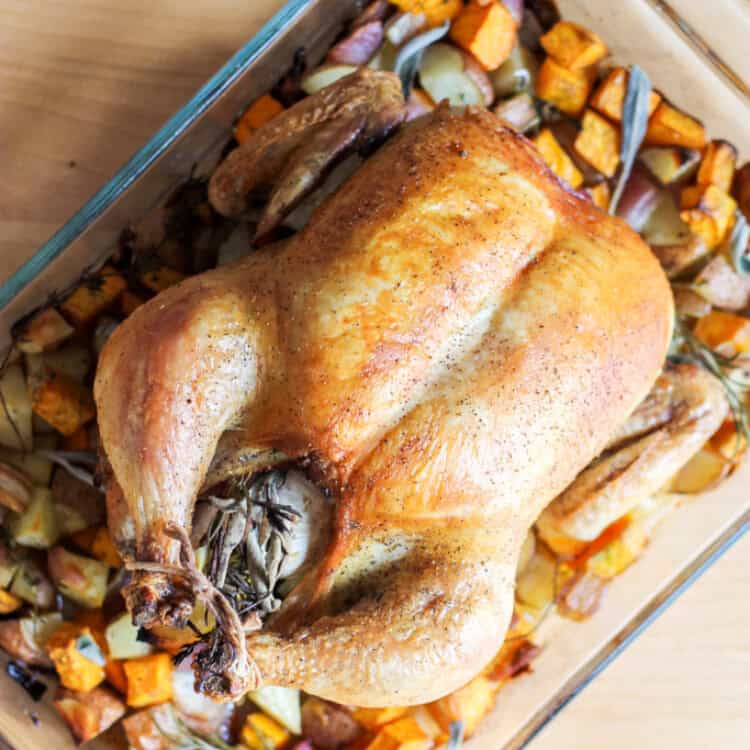 Roasted Chicken on top of roasted veggies in a glass baking dish.