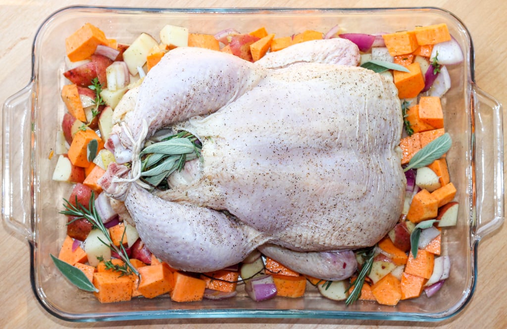 a seasoned and stuffed whole chicken on a bed of root vegetables in a roasting pan