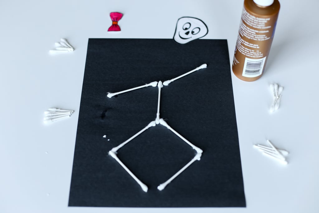 Assembling a Q-tip skeleton on black construction paper with craft glue and more Q-tips around it.