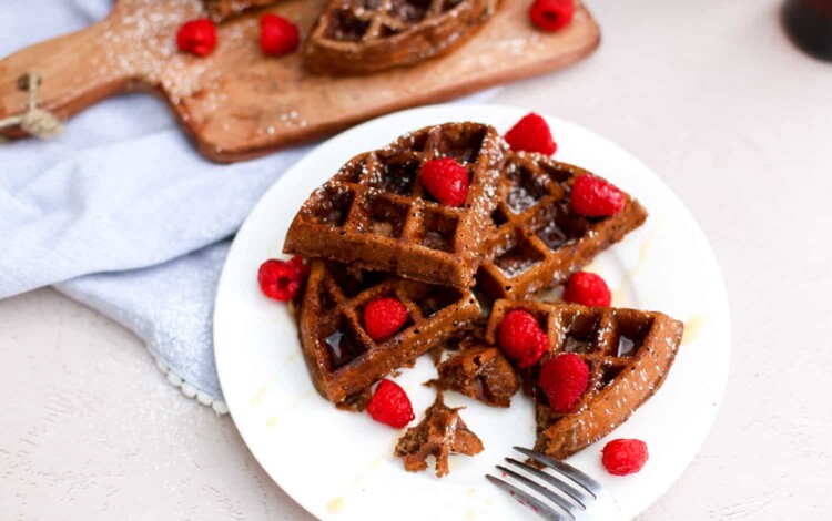 Cut up chocolate waffle on a plate with raspberries.