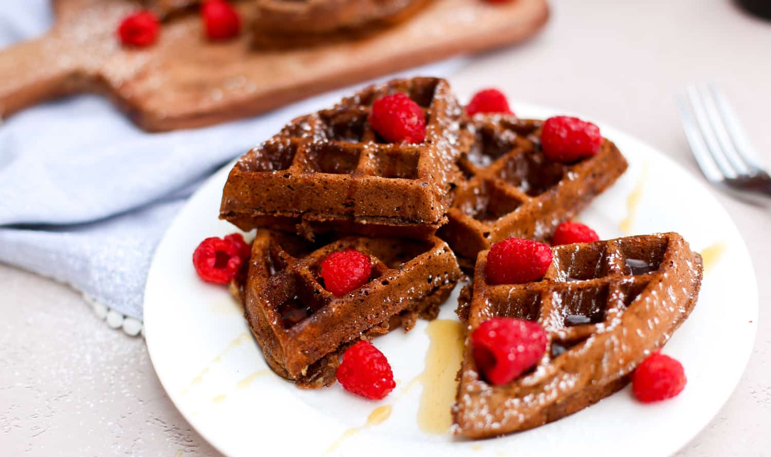 Chocolate waffles on a white plate with raspberries and poadered sugar on top.