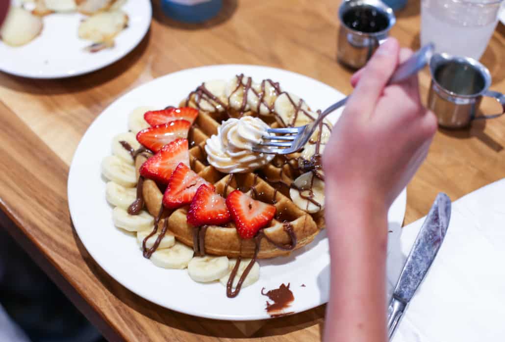 Belgian waffle with nutella, banana slices, strawberry slices, and whipped cream on a white plate