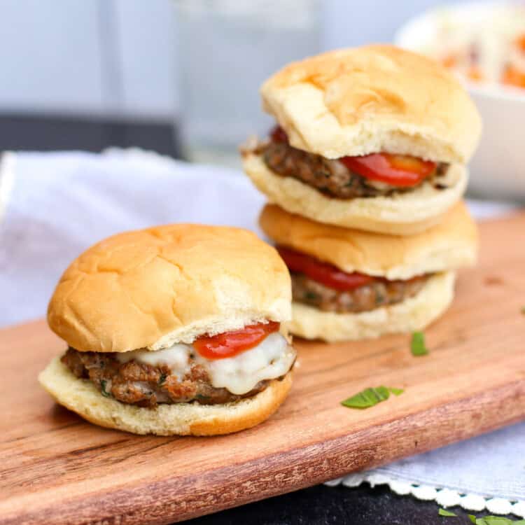 Italian sliders stacked up on a wooden cutting board.