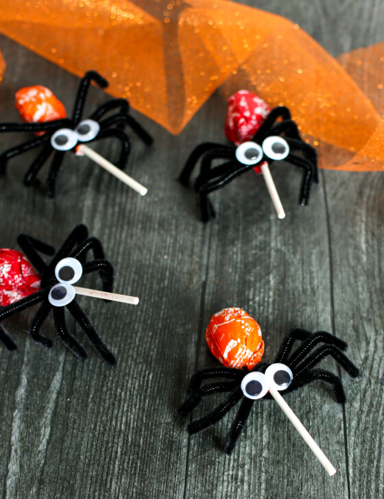 Spider Lollipops made from pipe cleaners and tootsie roll pops lined up on a wooden table.