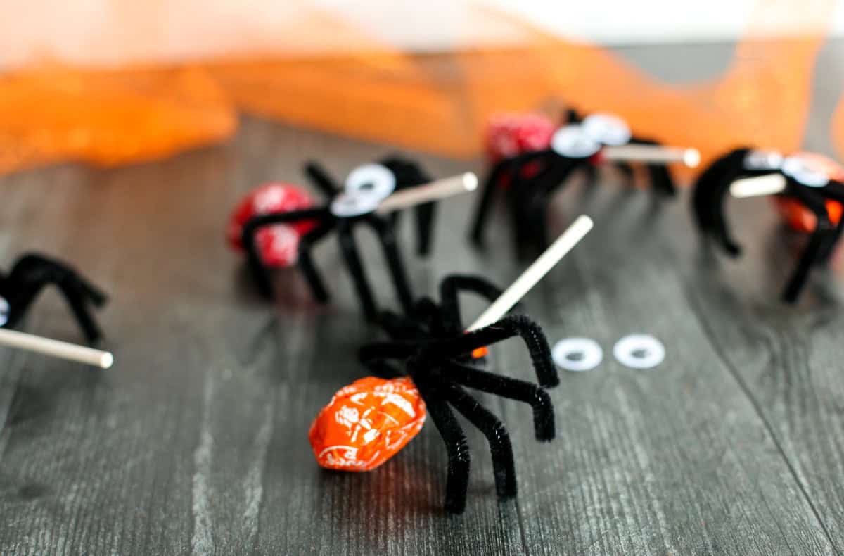 Spider lollipops lined up on a wooden table.