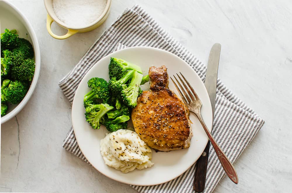 pan seared pork chop on a white plate with mashed potatoes and broccoli