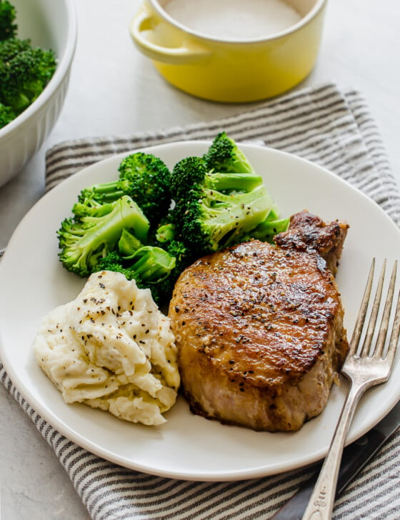 pan seared pork chop on a white plate with mashed potatoes and broccoli
