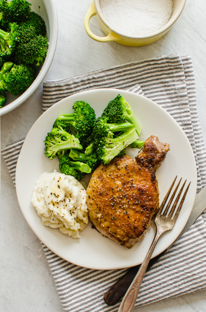 pan seared pork chop on a white plate with mashed potatoes and broccoli