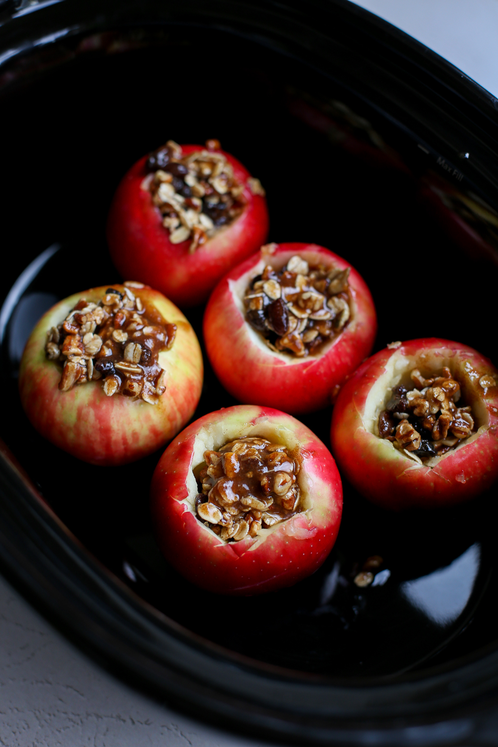 Uncooked cored apples with a filling in the middle being prepped to cook in the slow cooker.