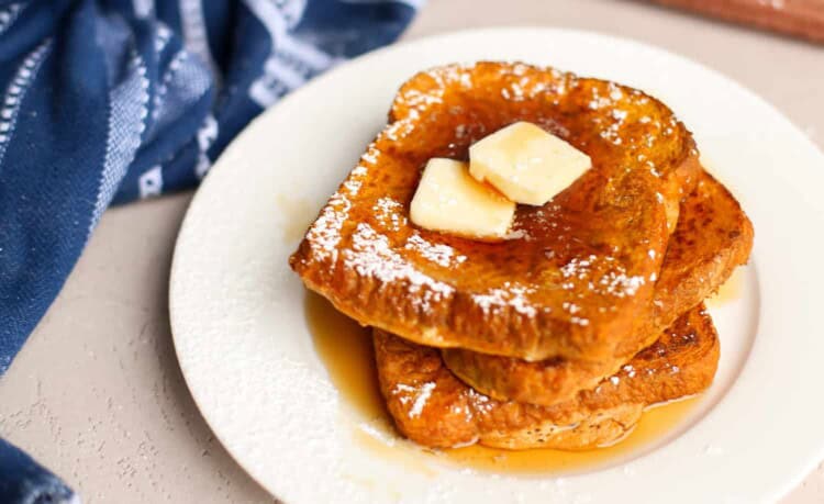 Pumpkin French toast slices stacked on a plate with syrup and a pat of butter on top.