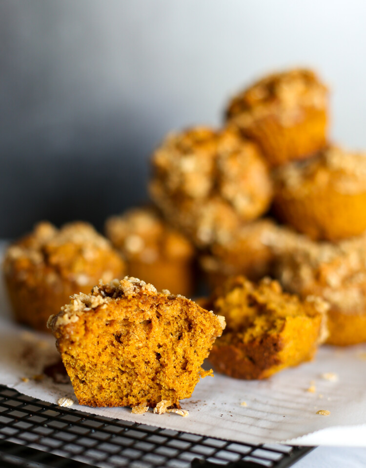 A pumpkin spice muffin cut in half on a baking rack with more muffins stacked up in the background.