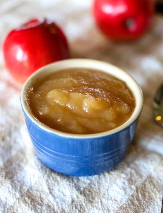 Slow cooker applesauce in a small blue bowl with a spoon next to it and apples in the background.
