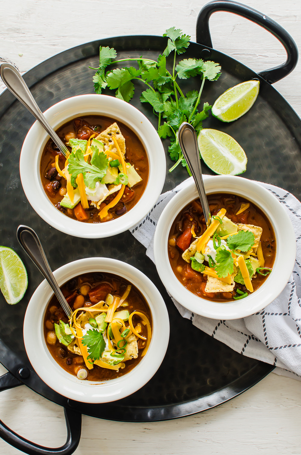Three bowls of chili with toppings like tortilla chips, avocado, cilantro, lime wedges, and cheese.