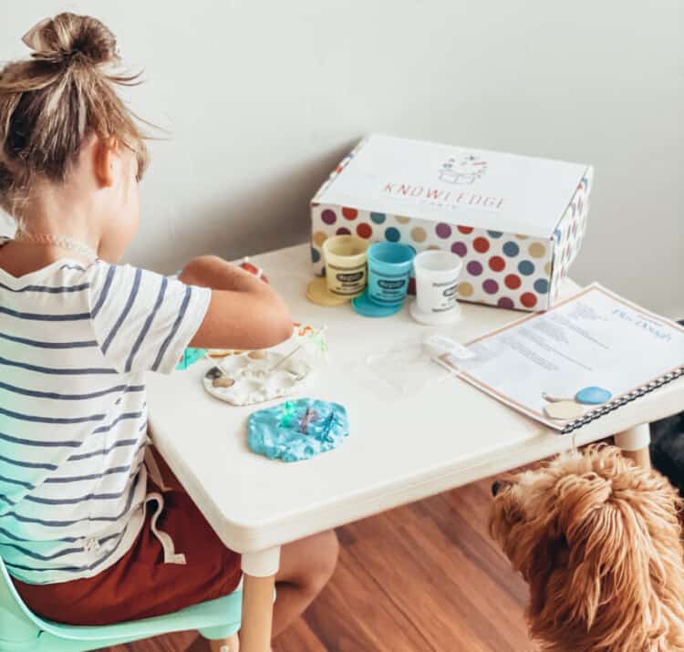 Child working at a small table on a project with a box that says Knowledge Crates on it sitting nearby.