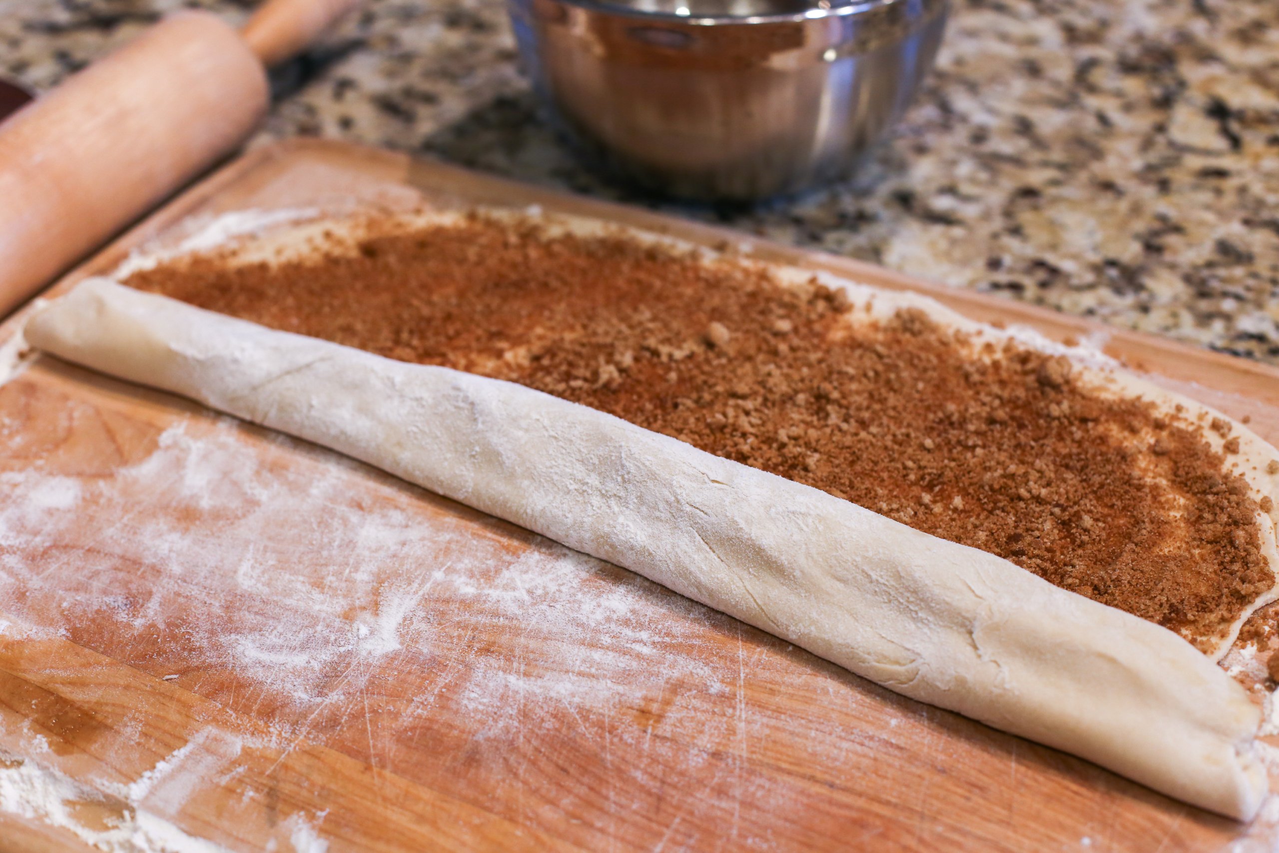 Cinnamon roll dough with a cinnamon-sugar mixture on top being rolled up before slicing.