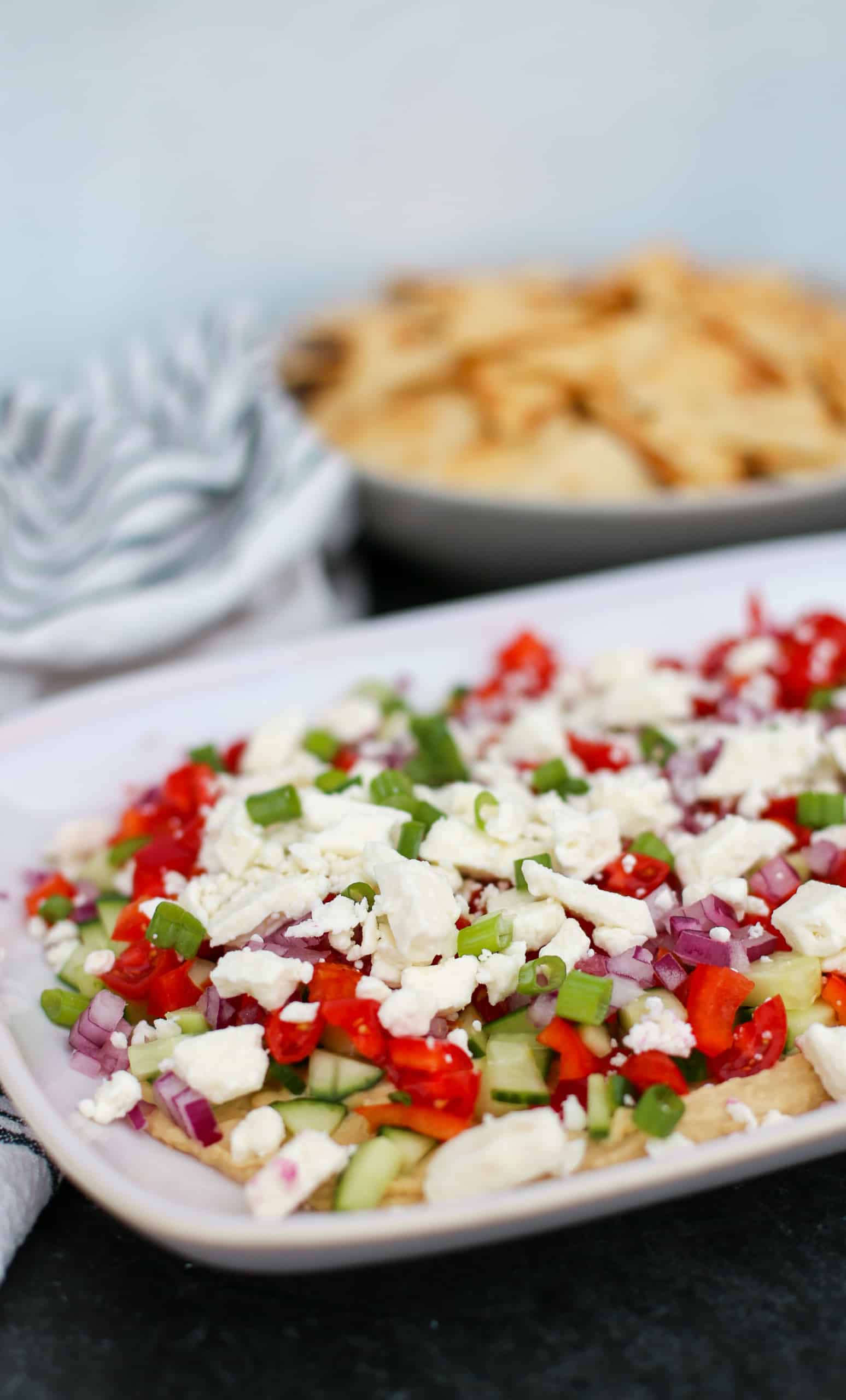 Greek dip on a platter with a bowl of pita crackers in the background.