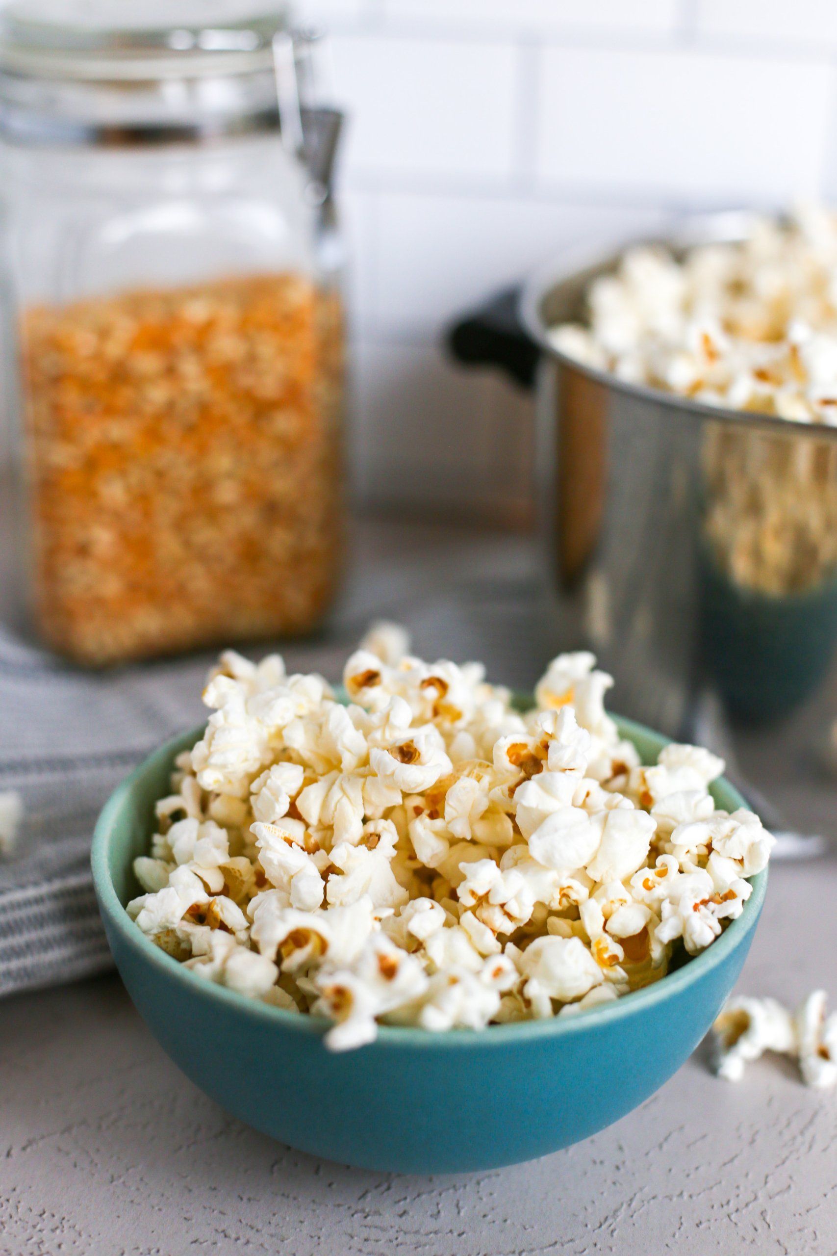 Homemade coconut oil popcorn in a blue bowl with a pot of more popcorn behind it.