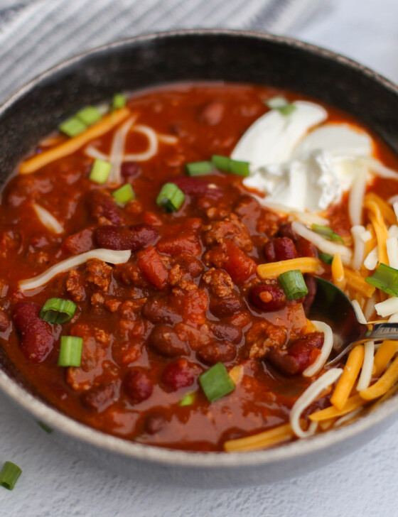 Bowl of instant pot chili with a dollop of sour cream, chopped chives, and shredded cheese on top.