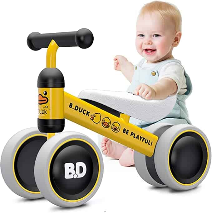 A toddler balance bike in yellow in black with 4 wheels and wide banana seat.