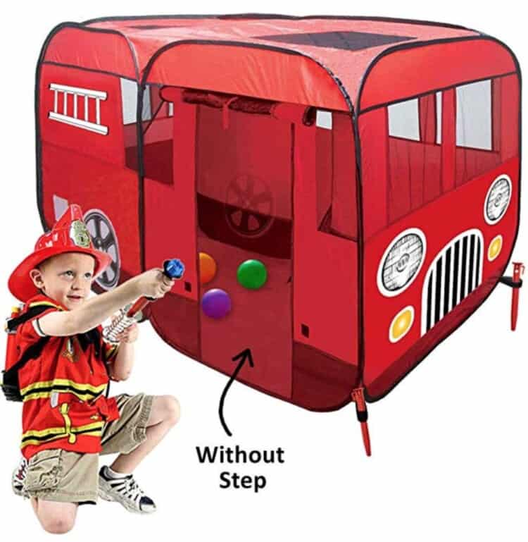 Pop-up playhouse that looks like a fire engine with a child dressed in play fireman's gear in front of it.