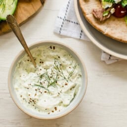 Tzatziki sauce in a white bowl with Greek pitas next to it.