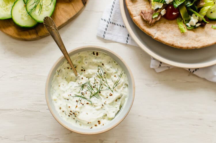 Tzatziki sauce in a white bowl with Greek pitas next to it.