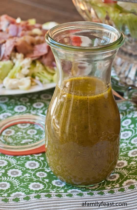 Jar of Greek dressing sitting in front of a Greek salad on a plate.