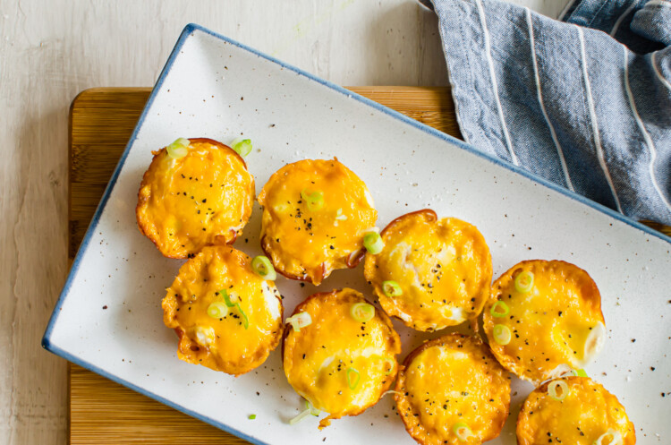 Ham and cheese egg cups on a white serving platter with sliced green onions on top.