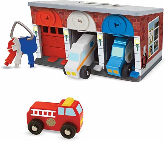 Wooden garage toy with three doors and a set of keys next to it - the red door is closed and a firetruck is parked out front; the white door is open and a white ambulance is coming out; the blue door is also open with a blue police car coming out.
