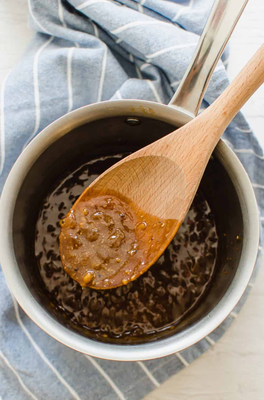 A wooden spoon stirring maple glaze in a saucepan to go over pork loin.