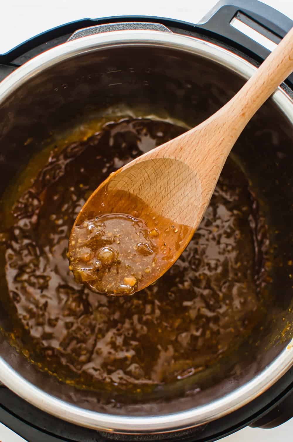 A wooden spoon taking some maple glaze out of the Instant Pot for Instant Pot pork loin.